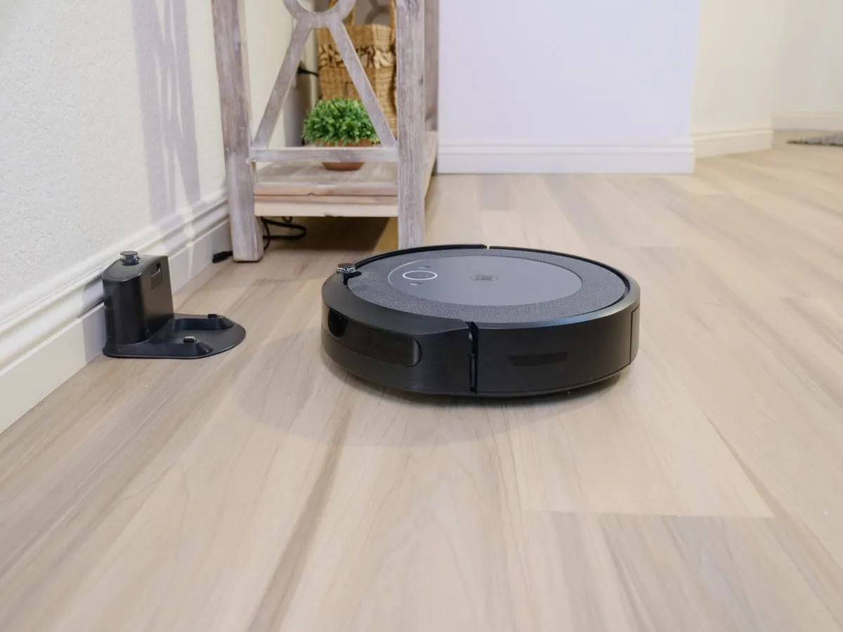 Aspirateur robot noir sur un parquet, à côté de sa station de charge